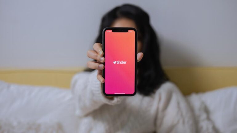 Woman holding up a phone with Tinder displayed.
