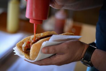 Hand putting sauce on sausage sandwich.